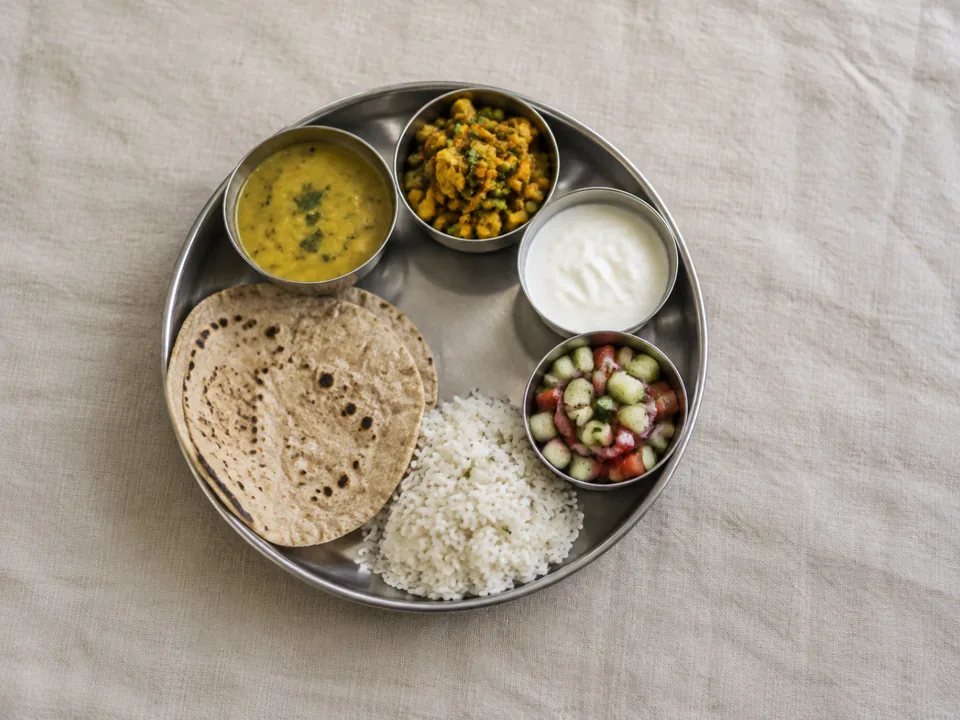 A home thali seen from above: one meal in several parts, with dal, sabzi, curd, salad, rotis and rice